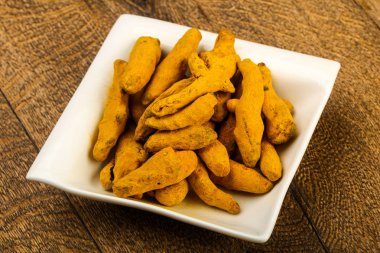 Tumeric kökü yığın içinde kase ahşap arka plan üzerinde