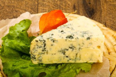 Ahşap arka planda salata yapraklı mavi peynir.