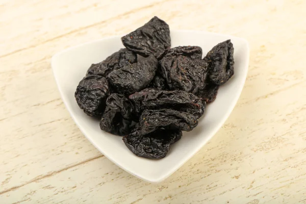 Dried plums heap in the bowl over wooden background