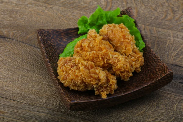 Crispy chicken wings with salad leaves on wood background