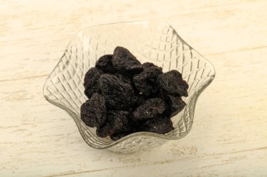 Kurumuş erikler ahşap arka planda kasede yığılıyor.