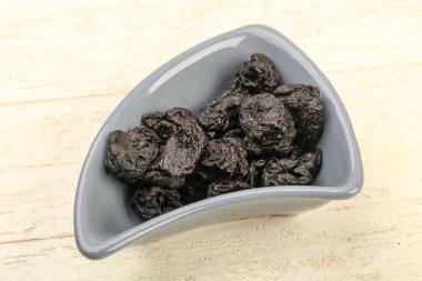 Kurumuş erikler ahşap arka planda kasede yığılıyor.