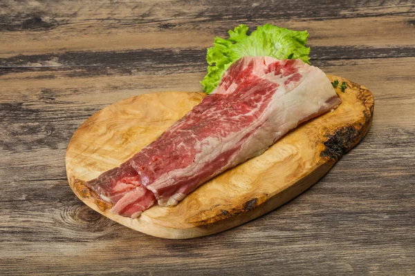 Raw beef bacon over wooden board served salad and thyme