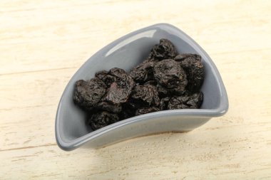 Kurumuş erikler ahşap arka planda kasede yığılıyor.