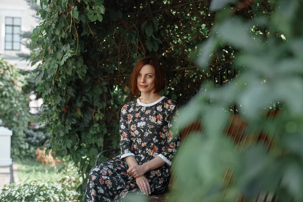 Красивая женщина, сидя на скамейке на фоне зеленых листьев — стоковое фото