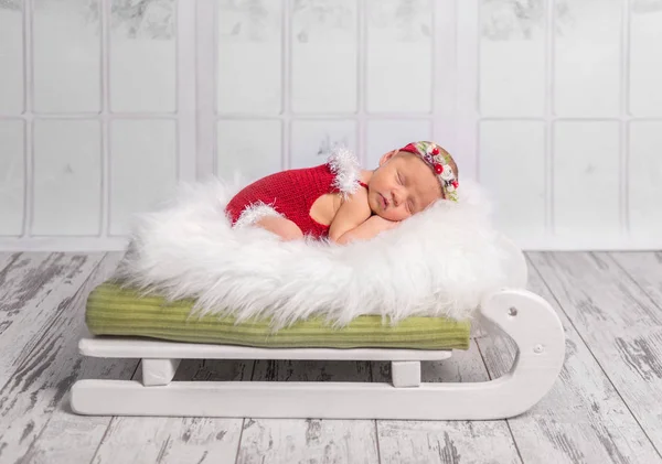 Nouveau-né en barboteuse rouge sur lit de traîneau — Photo
