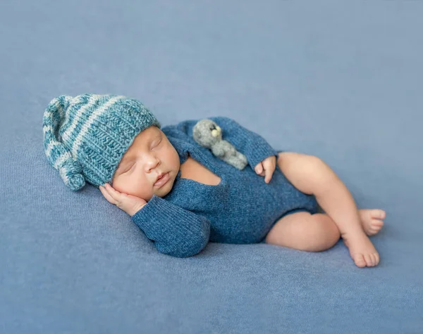 Slapende pasgeboren baby in blauwe jumpsuit en muts — Stockfoto