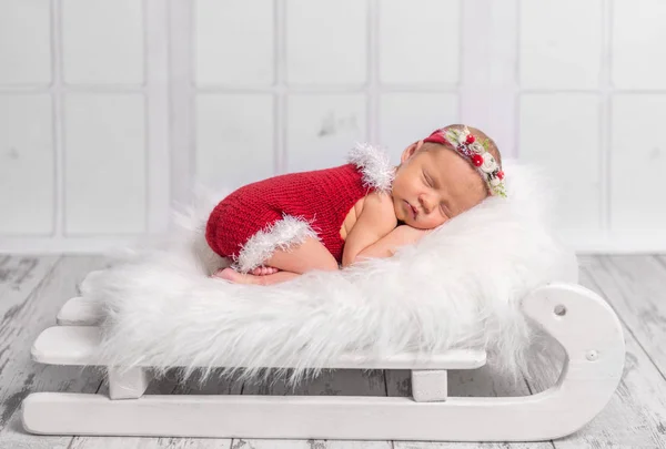 Beau nouveau-né en barboteuse rouge sur lit de traîneau — Photo