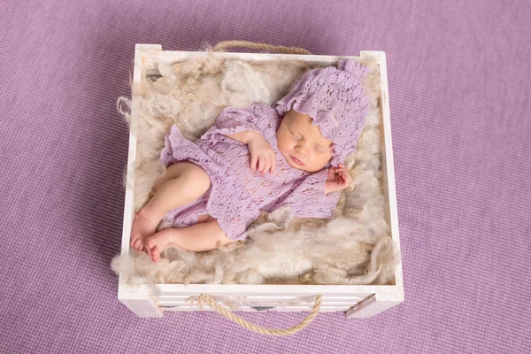Sweet newborn sleeping in square cot on violet background — Stock Photo, Image