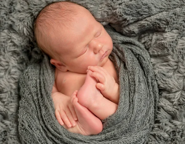 Säugling hält seine Füße, in eine Decke gehüllt, Nahaufnahme — Stockfoto