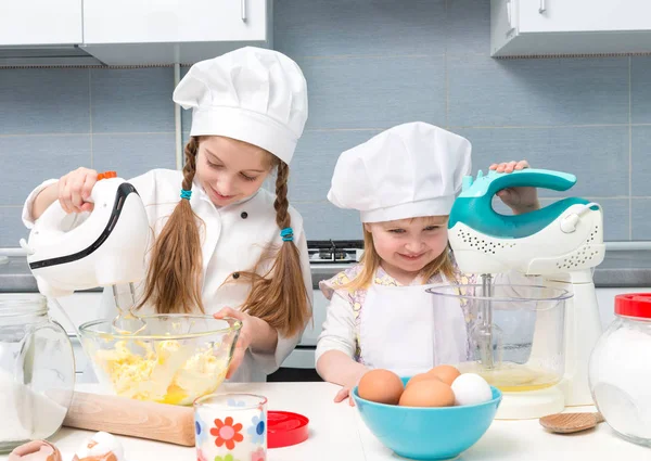 Zwei kleine Mädchen in Kochuniform mit Zutaten auf dem Tisch — Stockfoto