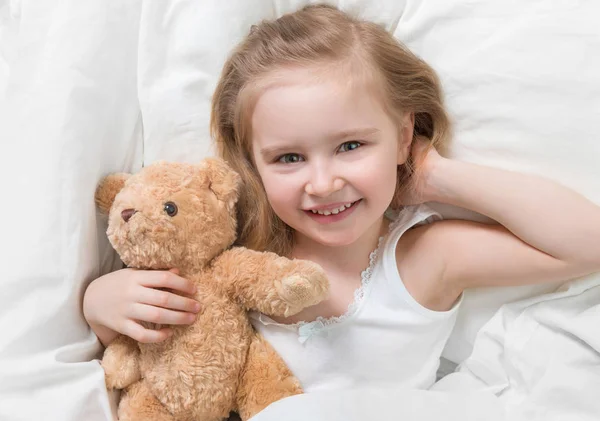 Dívka drží její hnědá teddy, v posteli — Stock fotografie