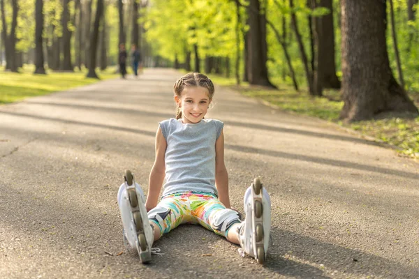 Girl rollerblading sitting on asphalt, stretching — Stock Photo, Image