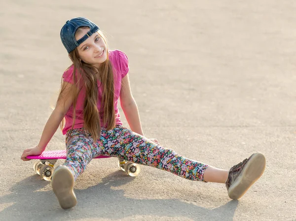 Menina com cabelos longos sentado na placa de patinação — Fotografia de Stock