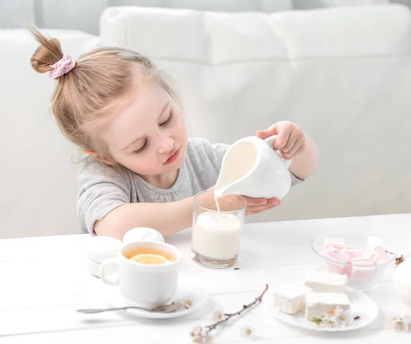 Liten flicka häller mjölk i hennes tekopp — Stockfoto