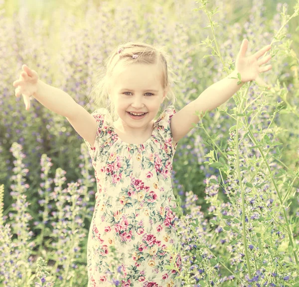 Child in field among flowers and herbs, smiling — Stock Photo, Image