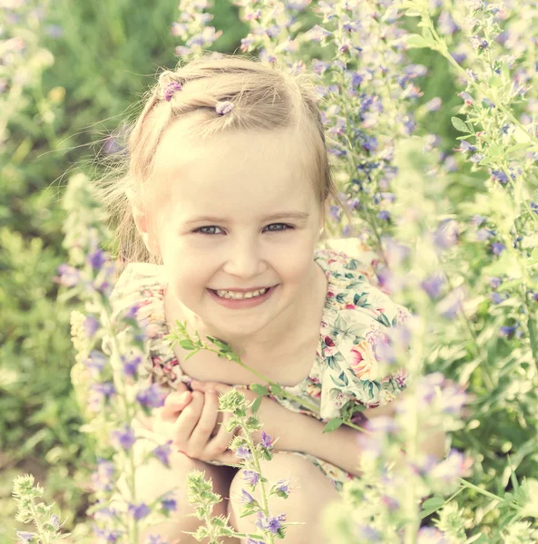 Meisje op gebied zit vol met kleine bloemen — Stockfoto