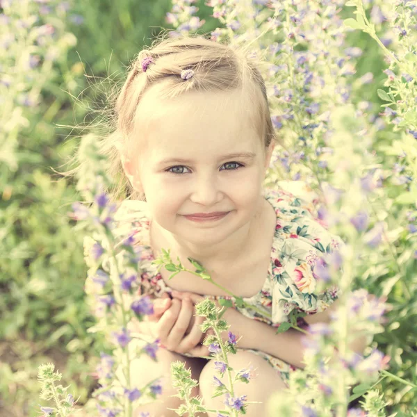 Meisje op gebied zit vol met kleine bloemen — Stockfoto