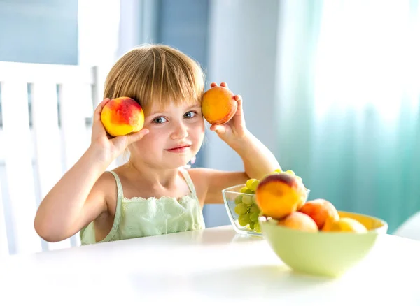 Menina bonito com pêssegos nas mãos na mesa — Fotografia de Stock