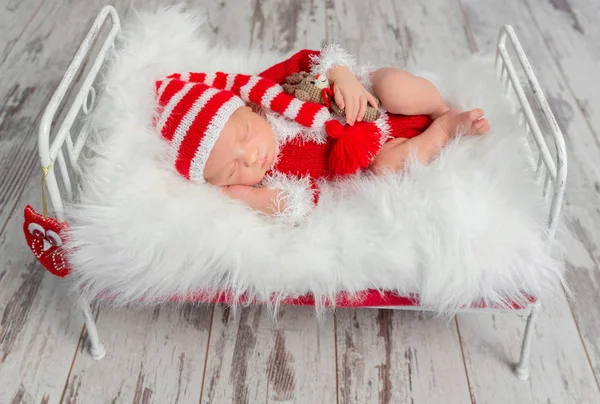 Niedliches schlafendes Baby mit rotem Hut auf kleinem Bett — Stockfoto