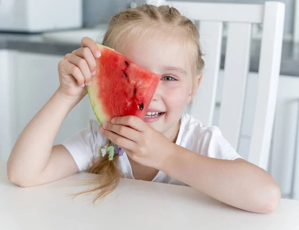 Schattig klein meisje eet een watermeloen in de keuken — Stockfoto