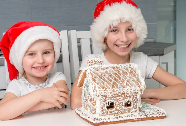 Deux sœurs souriantes au chapeau de Père Noël avec maison biscuite crémeuse — Photo
