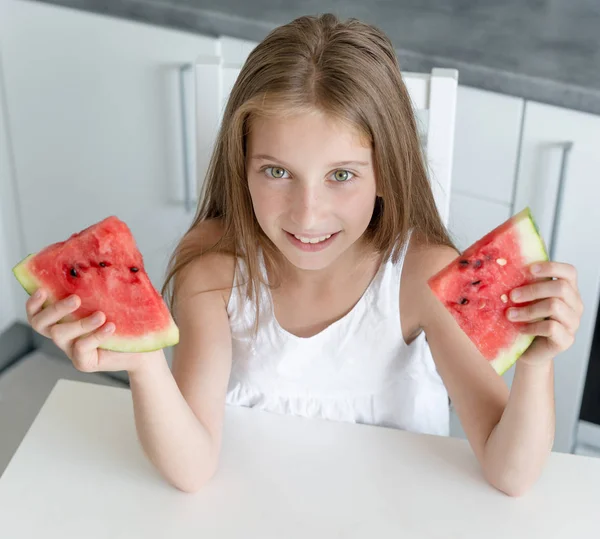 Schattig klein meisje eet een watermeloen in de keuken — Stockfoto