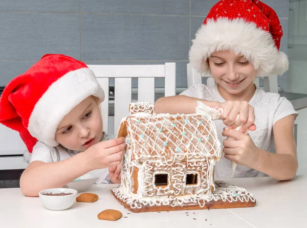 Two little sisters in santa hat making biscuit house — Stock Photo, Image