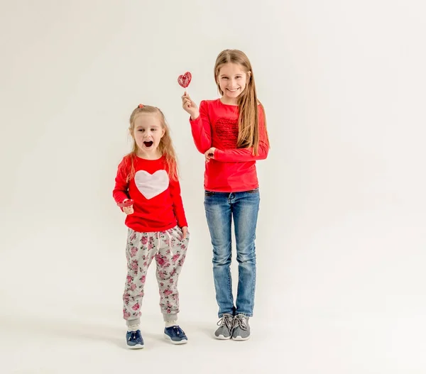 Dos hermanas lindas con piruletas en forma de corazón — Foto de Stock