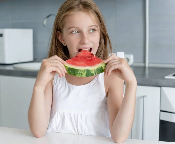 Süßes kleines Mädchen isst eine Wassermelone in der Küche — Stockfoto
