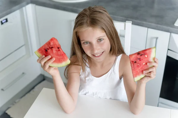 Söt liten flicka äter en vattenmelon i köket — Stockfoto