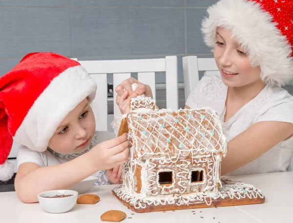 Két kis testvér Santa kalap így keksz ház — Stock Fotó
