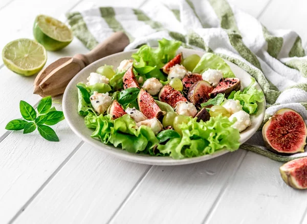 Salada com figos, mussarela e uvas em um fundo de madeira branco . — Fotografia de Stock