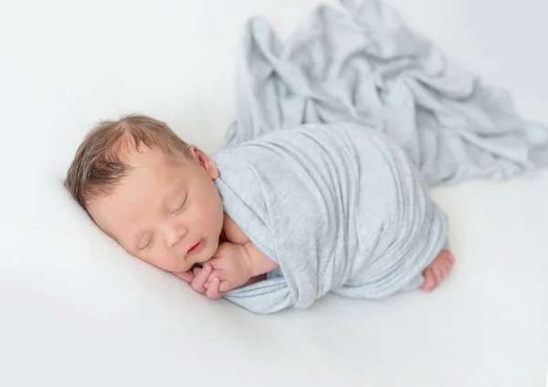 Pasgeboren baby in een licht blauwe wrap ingebakerd slapen — Stockfoto