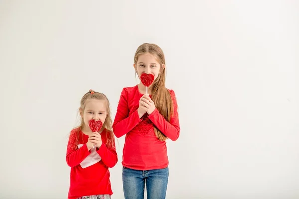 Dos hermanas lindas con piruletas en forma de corazón —  Fotos de Stock