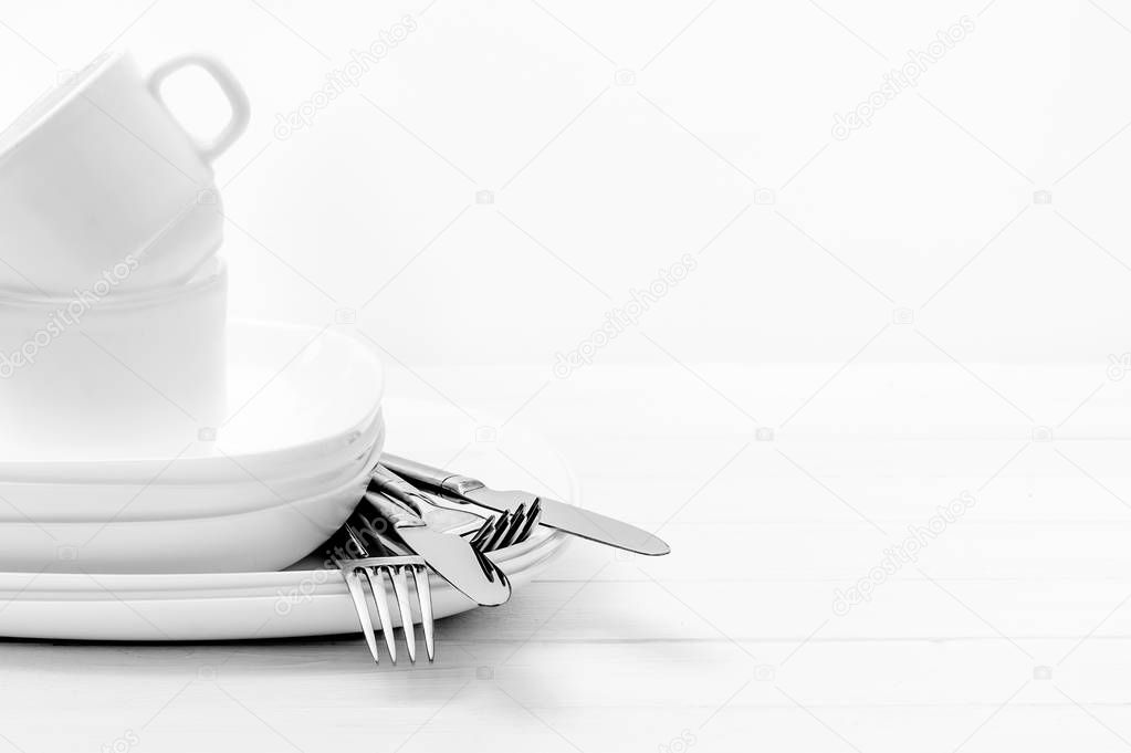 Plates, cups and silver cutlery on light white background