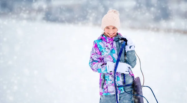 Menina no traje de esqui segurando trenós — Fotografia de Stock