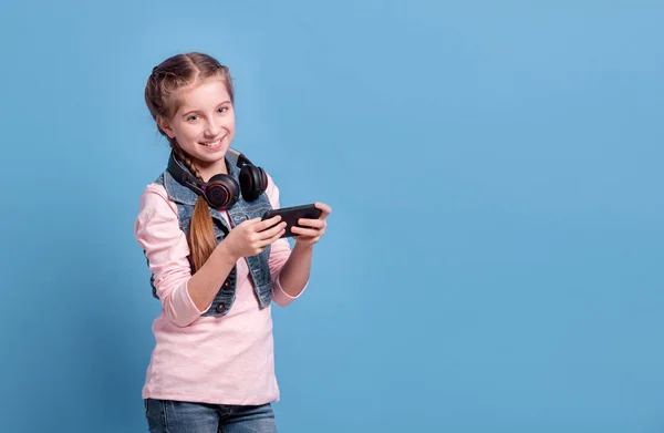 Adolescente jugando con el teléfono inteligente sobre fondo azul — Foto de Stock
