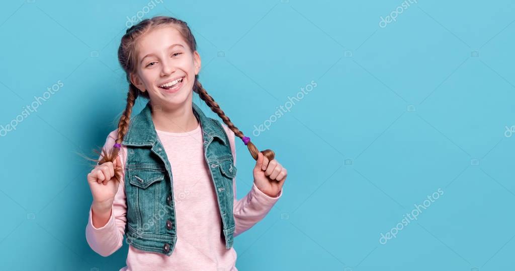 Fun teenage girl with open mouth holding her long french braids. Positive and cheerful emotions