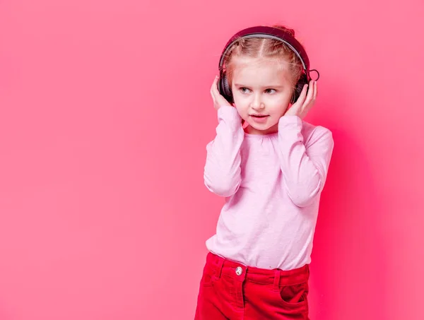 Niña en auriculares sobre fondo rosa — Foto de Stock