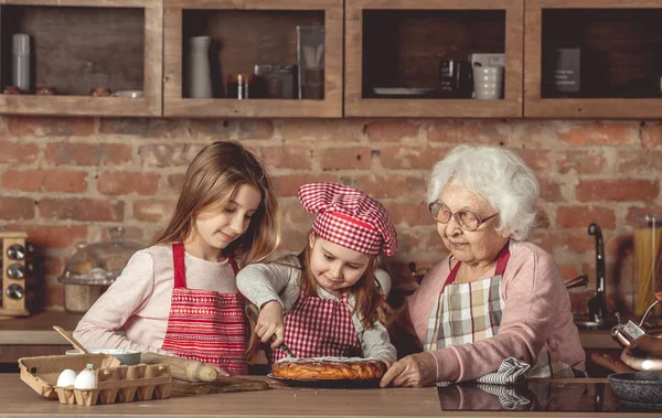 Oma met haar kleindochters proeverij taart — Stockfoto