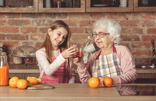 Granny with granddaughter tasting orange juice at kitchen — Stock Photo, Image