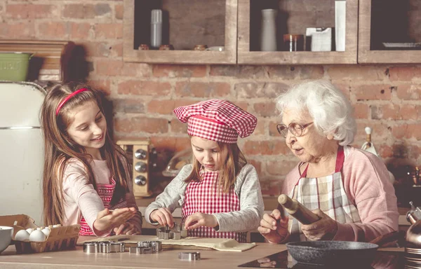 Little granddaughters help granny to bake cookies — Stock Photo, Image
