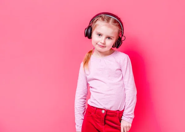 Niña en auriculares sobre fondo rosa — Foto de Stock