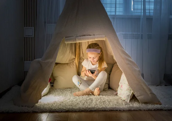 Menina com smartphone sentado na tenda teepee — Fotografia de Stock