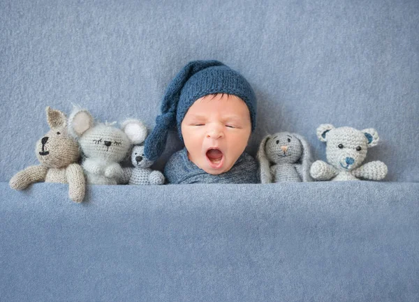 Newborn baby boy yawning and lying between plush toys — Stock Photo, Image