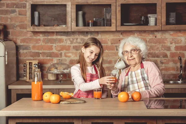 Avó com neta degustação de suco de laranja na cozinha — Fotografia de Stock