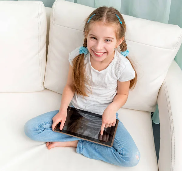 Fröhliches kleines Mädchen mit Tablet an den Beinen, das in die Kamera schaut — Stockfoto