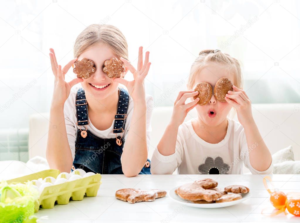 Happy little girls holding Easter cookies in front of their eyes