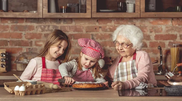 Oma met haar kleindochters proeverij taart — Stockfoto